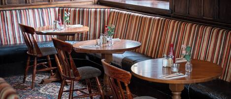 Un acogedor interior de restaurante con asientos acolchados a rayas, mesas de madera y una alfombra estampada.