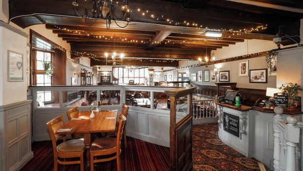A restaurant with a wooden interior, a bar area, and a seating area with a red carpet. - Bridge Inn Hotel  by Greene King Inns (Wirral)
