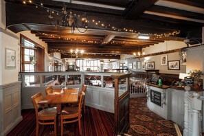 A restaurant with a wooden interior, a bar area, and a seating area with a red carpet. - Bridge Inn Hotel  by Greene King Inns (Wirral)