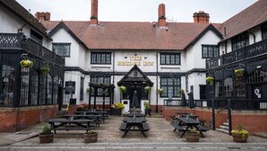 A traditional inn with a white facade, black-framed windows, and a sign reading "The Bridge Inn". There are outdoor tables and potted plants around the entrance. - Bridge Inn Hotel  by Greene King Inns (Wirral)