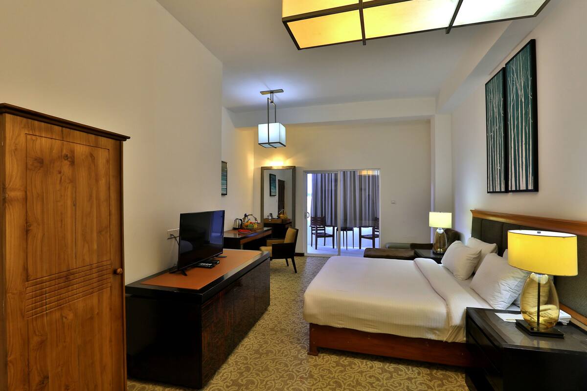 A hotel room with a bed, desk, television, and a view of the outside.
