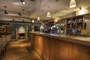 Un espace bar avec un comptoir en bois, des étagères remplies de bouteilles et une cheminée.
