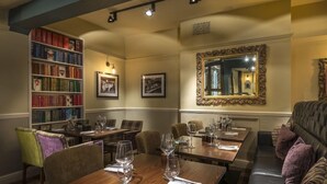 Zona pranzo con diversi tavoli, sedie, una libreria e un grande specchio decorativo.