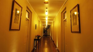 A hallway with framed pictures on the walls, a staircase at the end, and a table with flowers in the center. - The Firs (Nuwara Eliya)