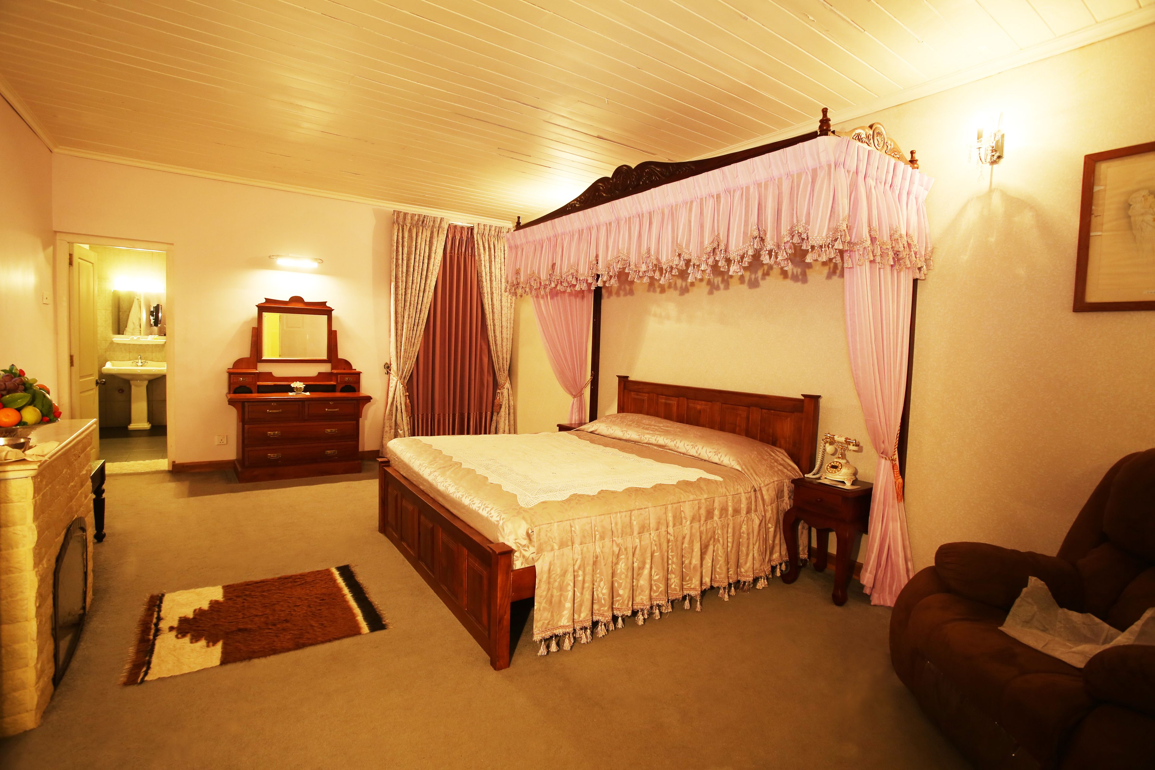 A bedroom with a four-poster bed, a wooden dresser, a nightstand, and a brown leather armchair.