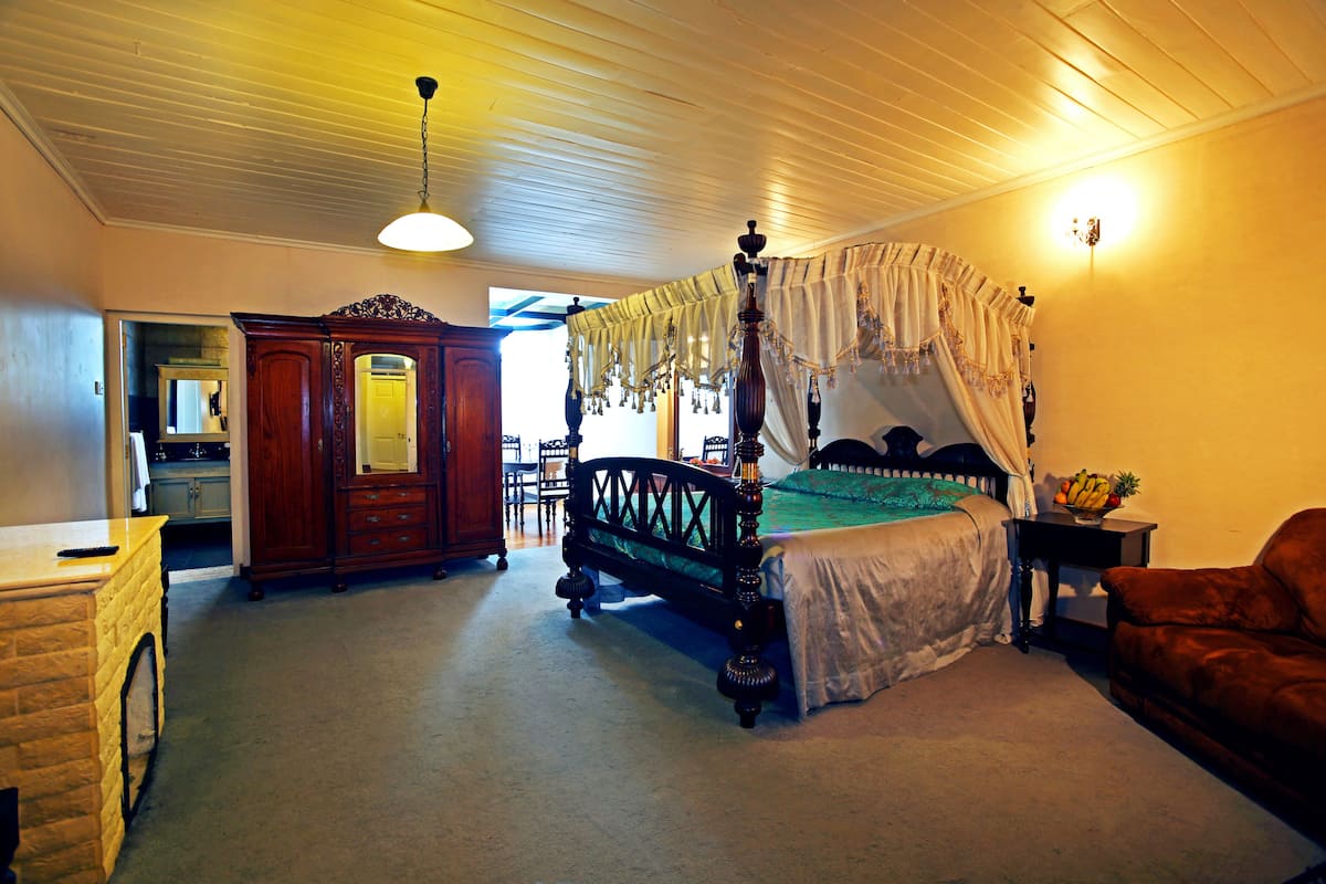 A spacious bedroom with a four-poster bed, a wooden dresser, and a nightstand with a lamp.