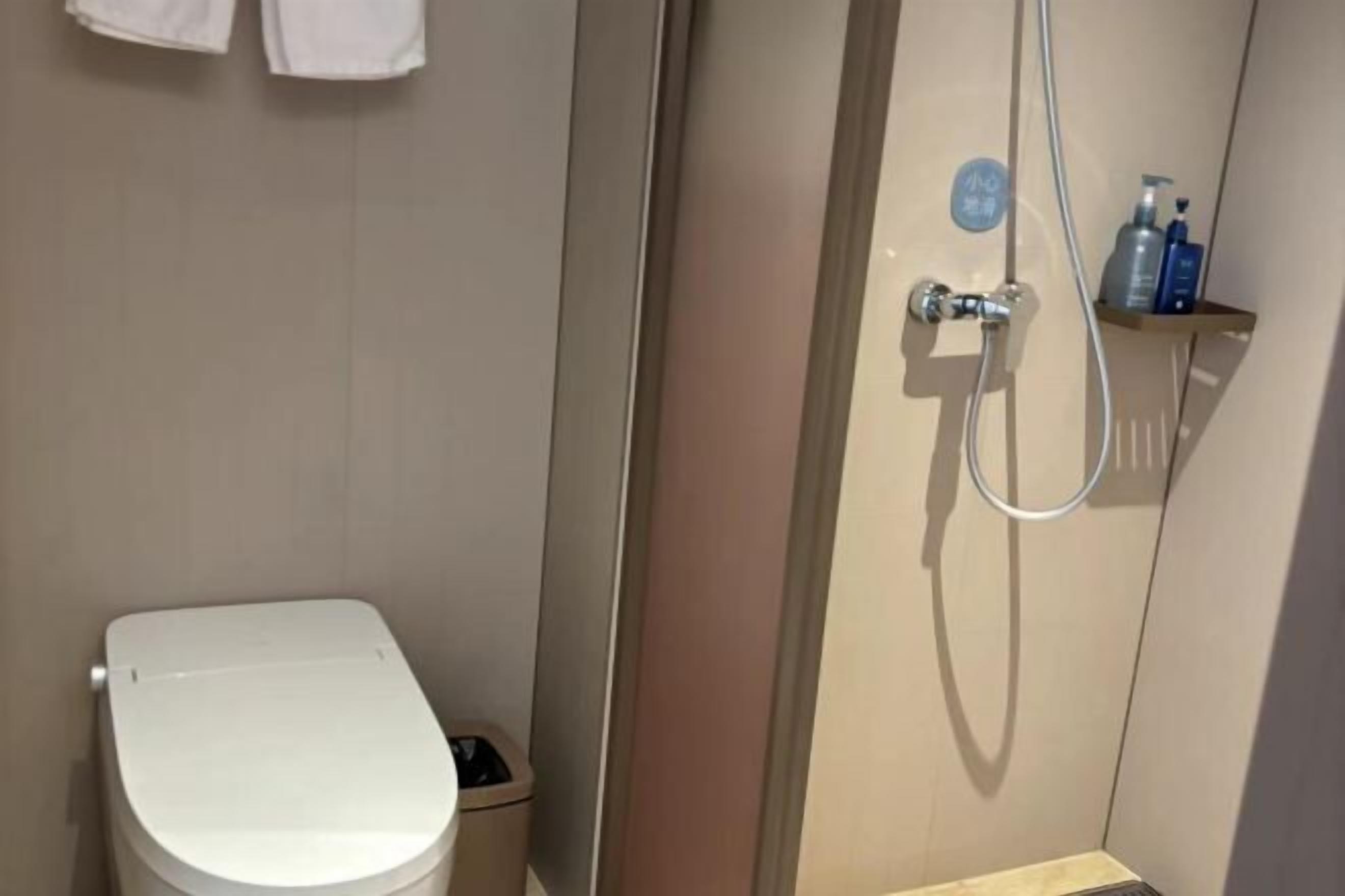 A bathroom with a toilet, a shower area, and a shelf with toiletries.
