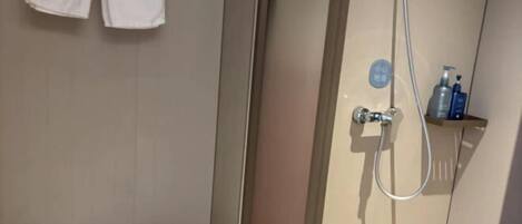 A bathroom with a toilet, a shower area, and a shelf with toiletries.