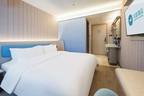 A hotel room with a large bed, a bedside table, a small desk, and a bathroom with a sink and mirror. - Hanting Express (Yangzhou Wenchang Ge) (Yangzhou)