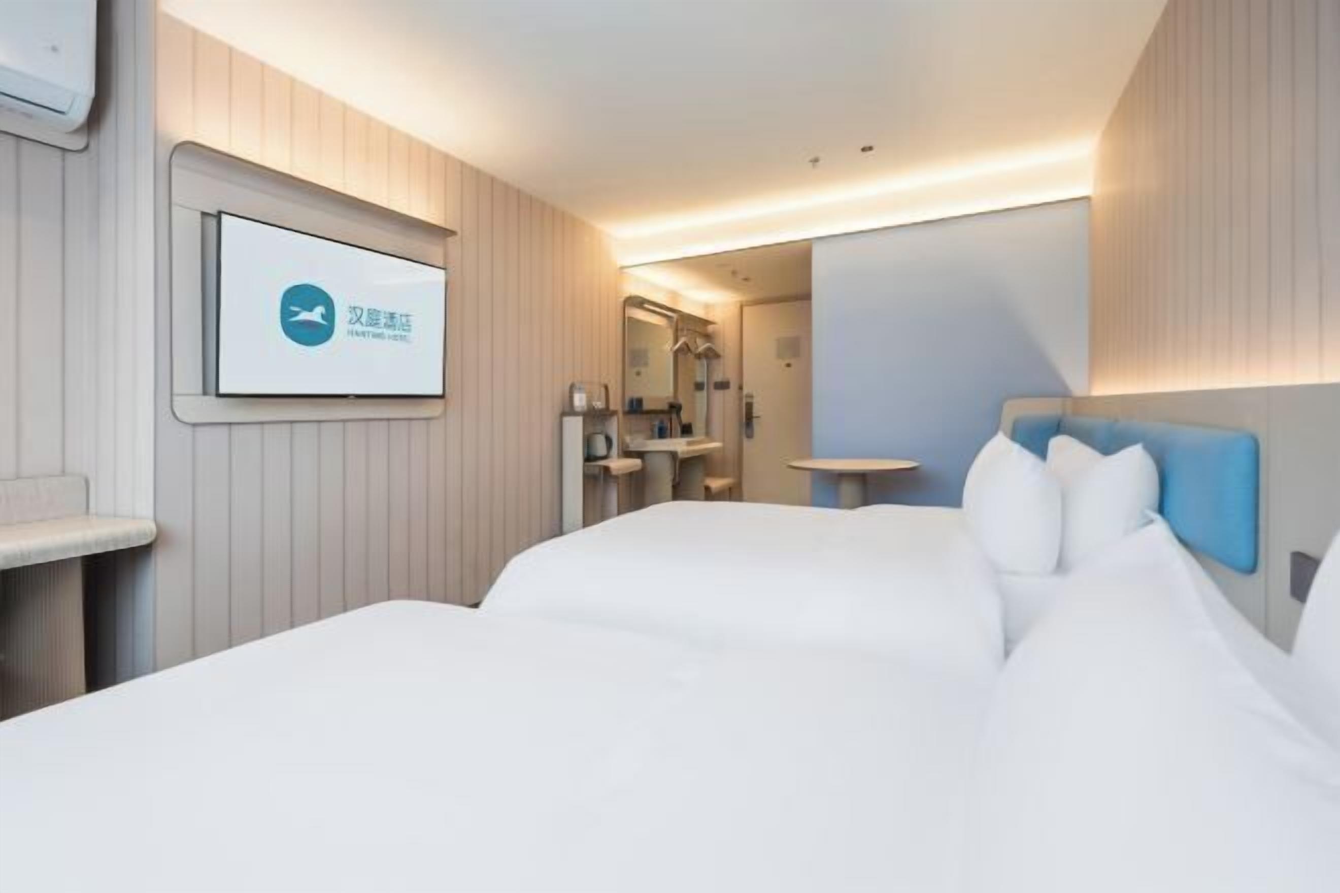 A hotel room with a bed, a small table, a mirror, and a TV screen displaying a logo.