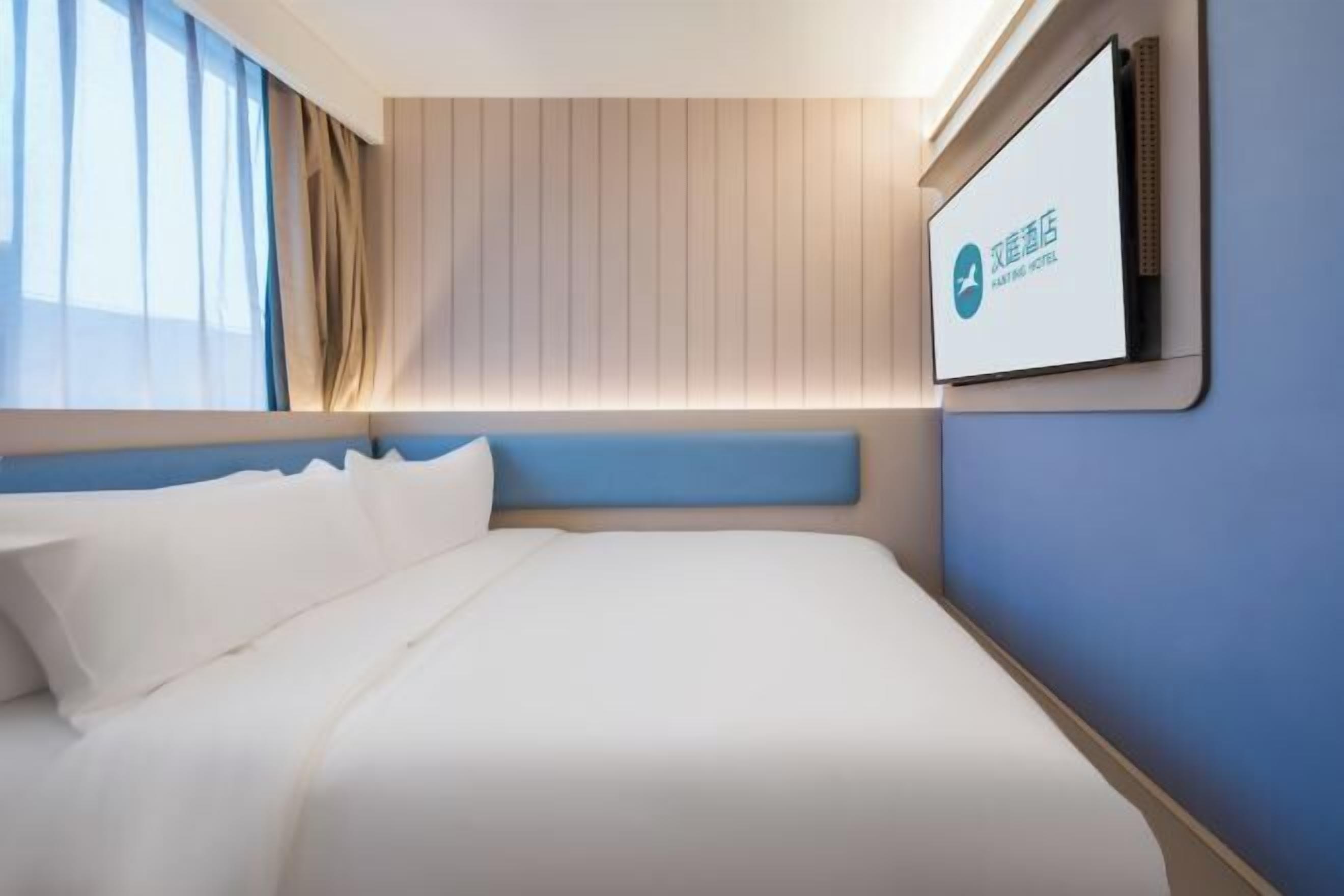 A modern hotel room with a large bed, a mounted television, and a window with curtains.