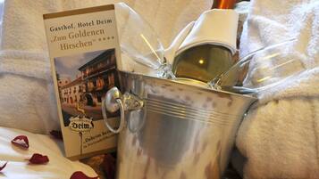 A bed with rose petals, a bottle of champagne, and a book titled "Zum Goldenen Hirschchen".