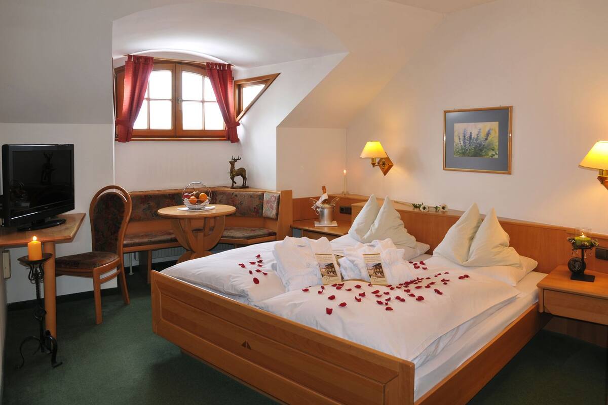 Ein Hotelzimmer mit Bett, Schreibtisch, Fernseher, einem Fenster mit Vorhängen und einem Gemälde an der Wand.