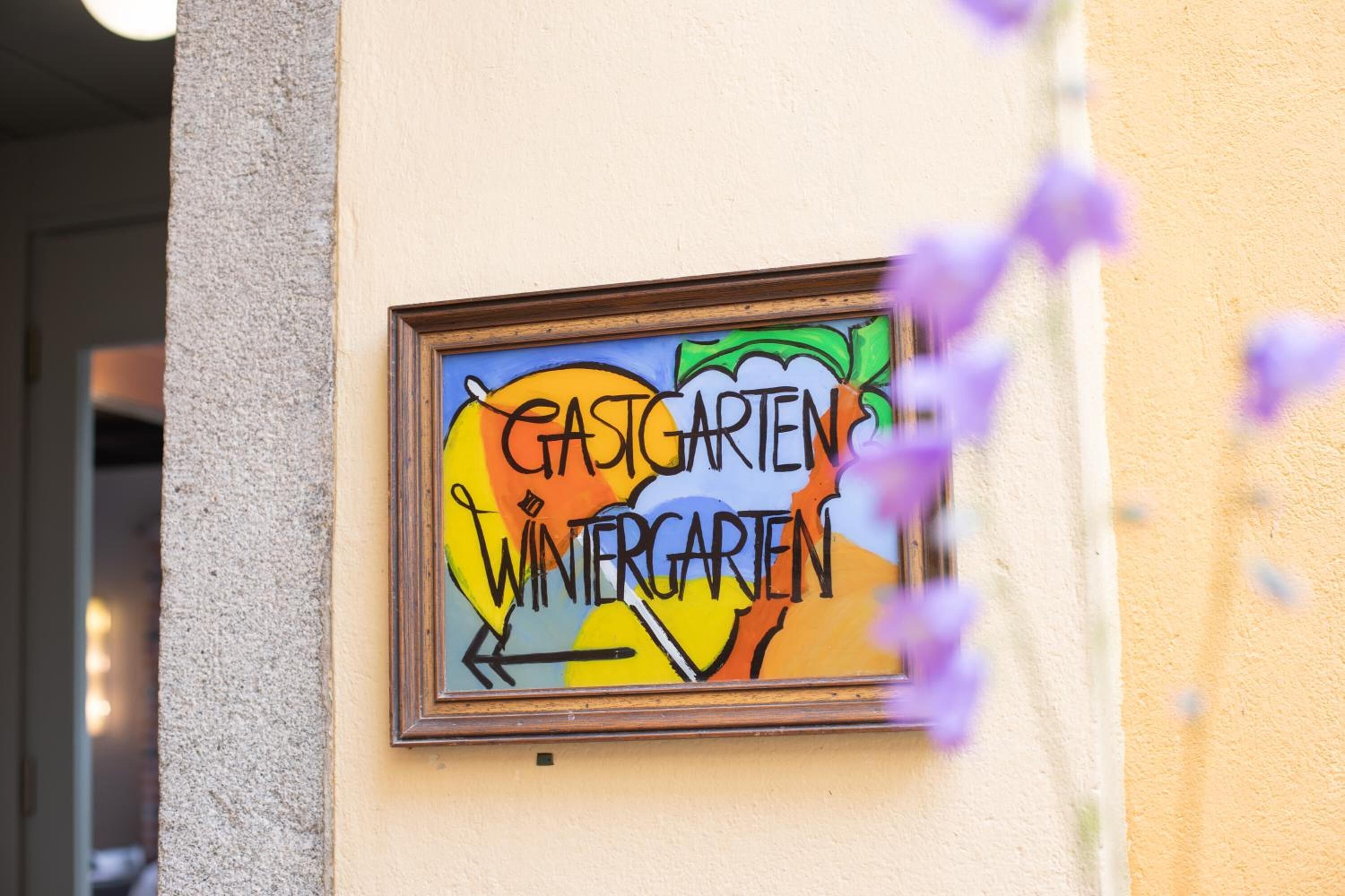 Une enseigne encadrée, affichée sur le mur d’un bâtiment, portant l’inscription « GASTGARTEN WINTERGARTEN ».