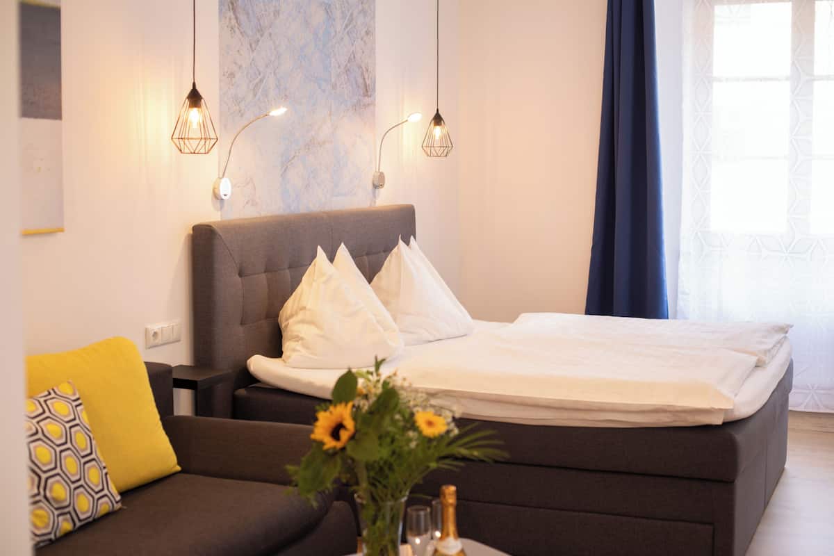 Ein modernes Hotelzimmer mit einem Bett, einem Schlafsofa und einem Nachttisch mit Blumen.