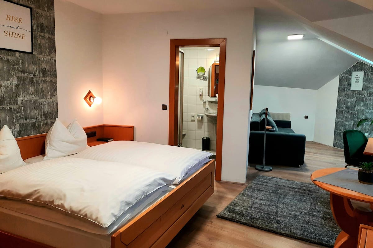 Ein modernes Hotelzimmer mit einem hölzernen Bett, einem Schreibtisch und Blick auf das Badezimmer und die Küche.