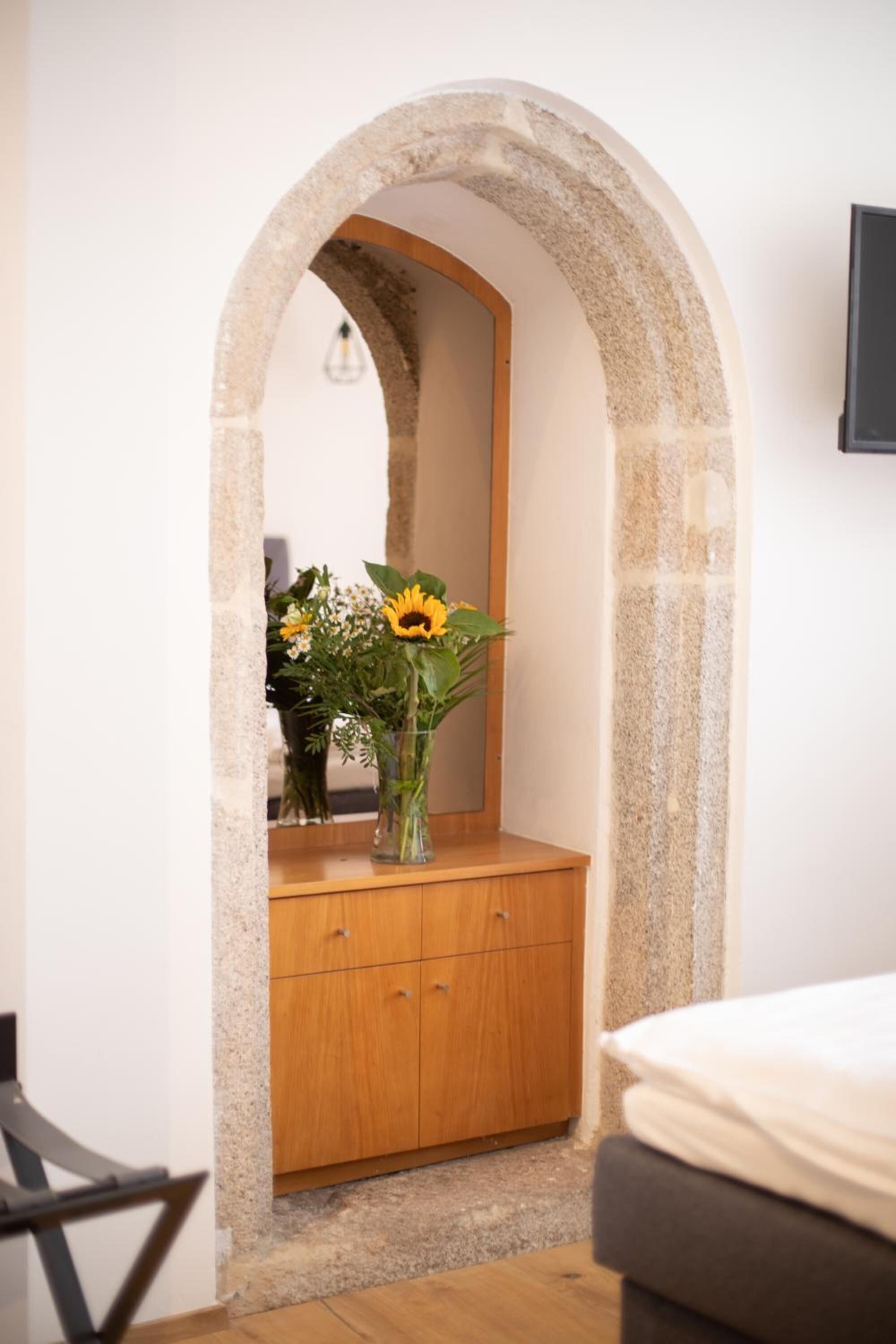 A bedroom with a wooden dresser, a mirror, and a vase with flowers.