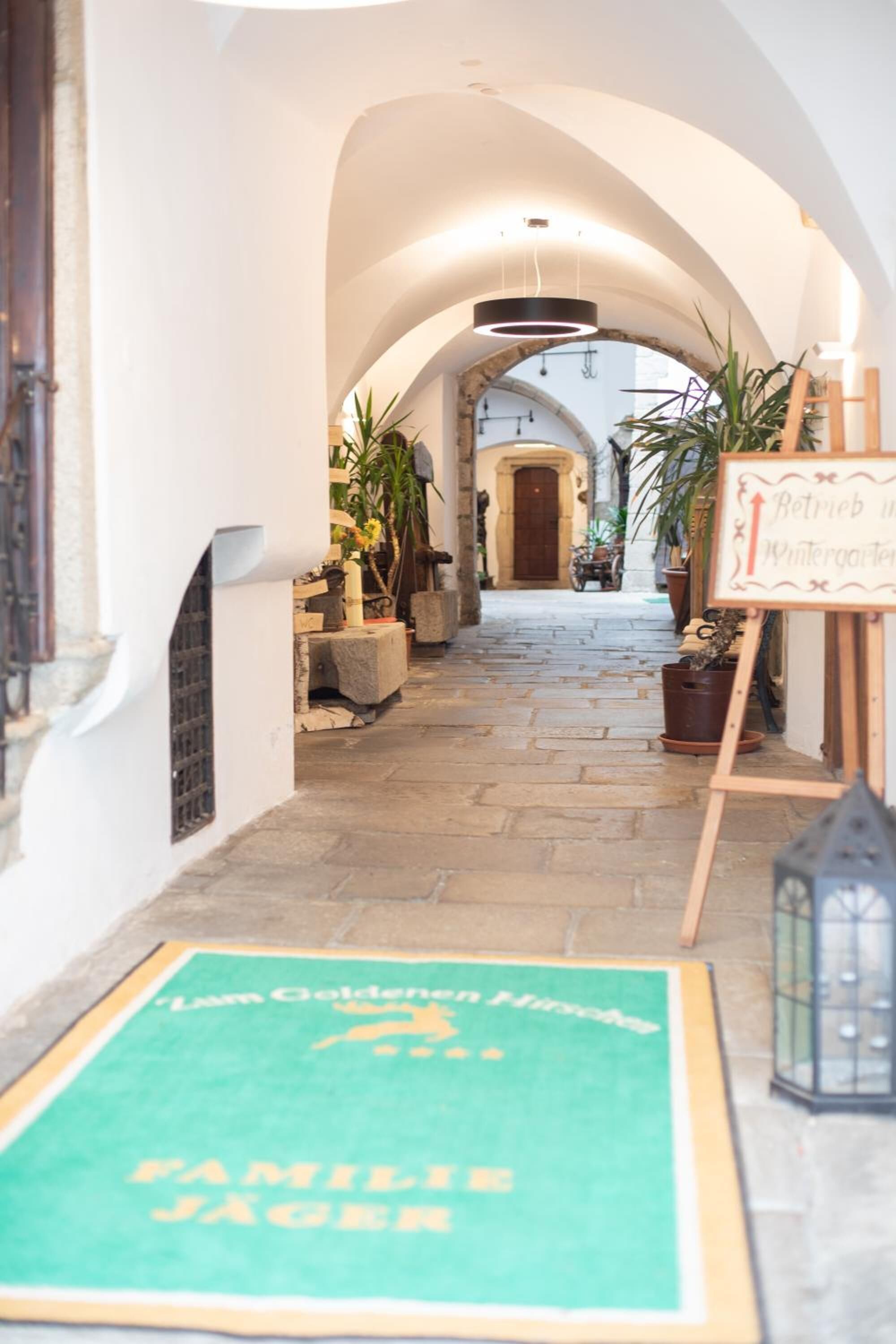 A narrow stone-paved corridor with arched ceilings, potted plants, and a signboard.