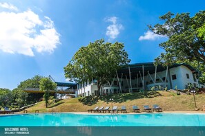 Un hotel con piscina, tumbonas y un árbol grande en primer plano.