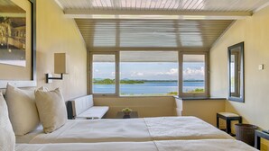 A bedroom with two beds, a bench, a small table with a plant, and a view of a lake. - EKHO Lake Polonnaruwa (Polonnaruwa)