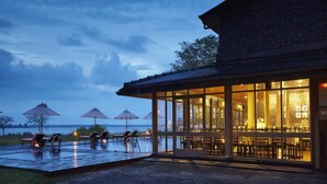 A building with a covered outdoor area, including a pool and lounge chairs, and a view of the water. - EKHO Lake Polonnaruwa (Polonnaruwa)