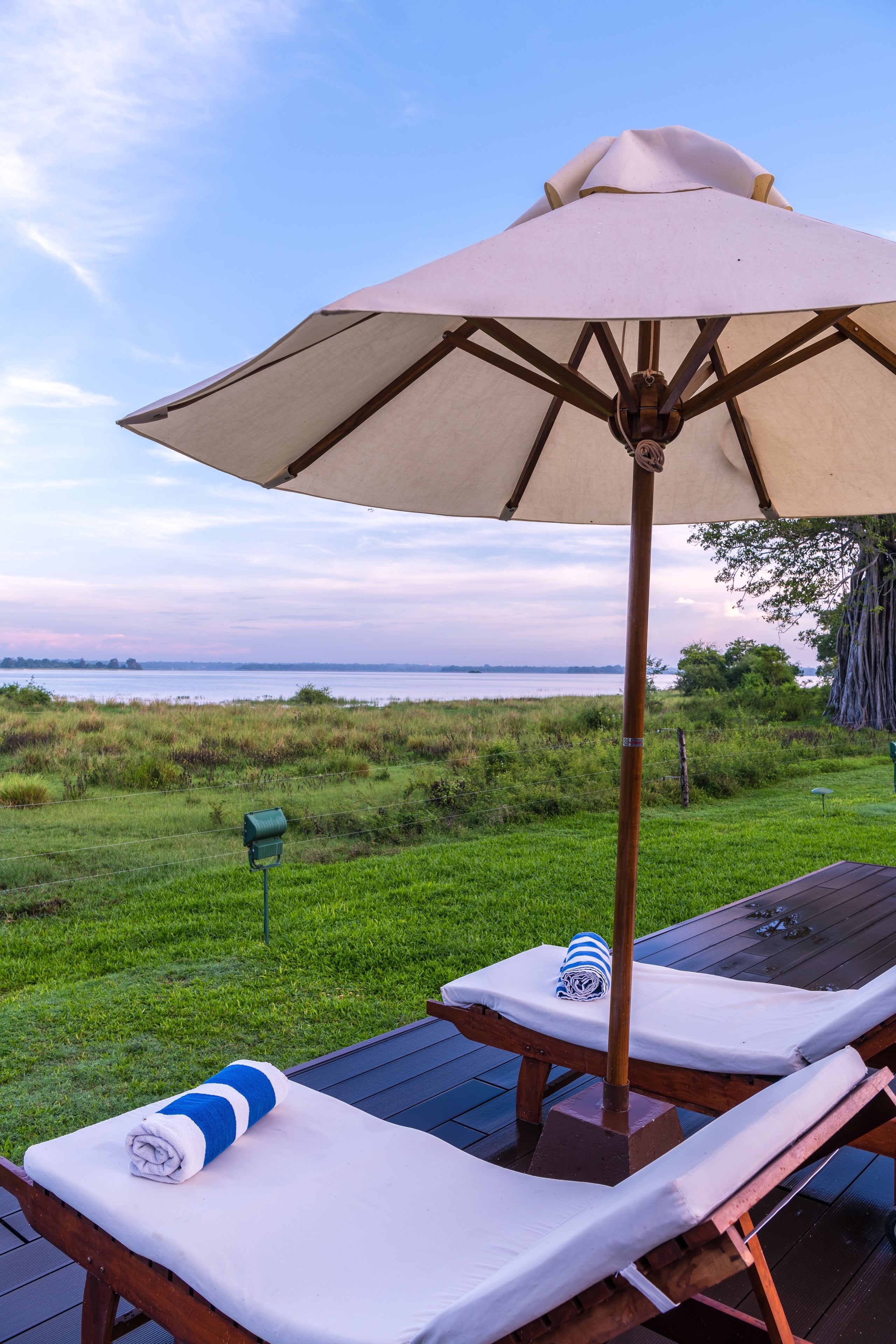 A deck with two lounge chairs, a large umbrella, and a view of the water.