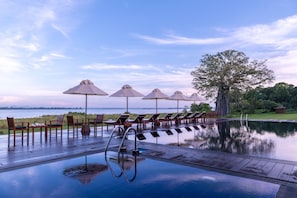 An infinity pool with lounge chairs and umbrellas, surrounded by a wooden deck and a view of the water. - EKHO Lake Polonnaruwa (Polonnaruwa)