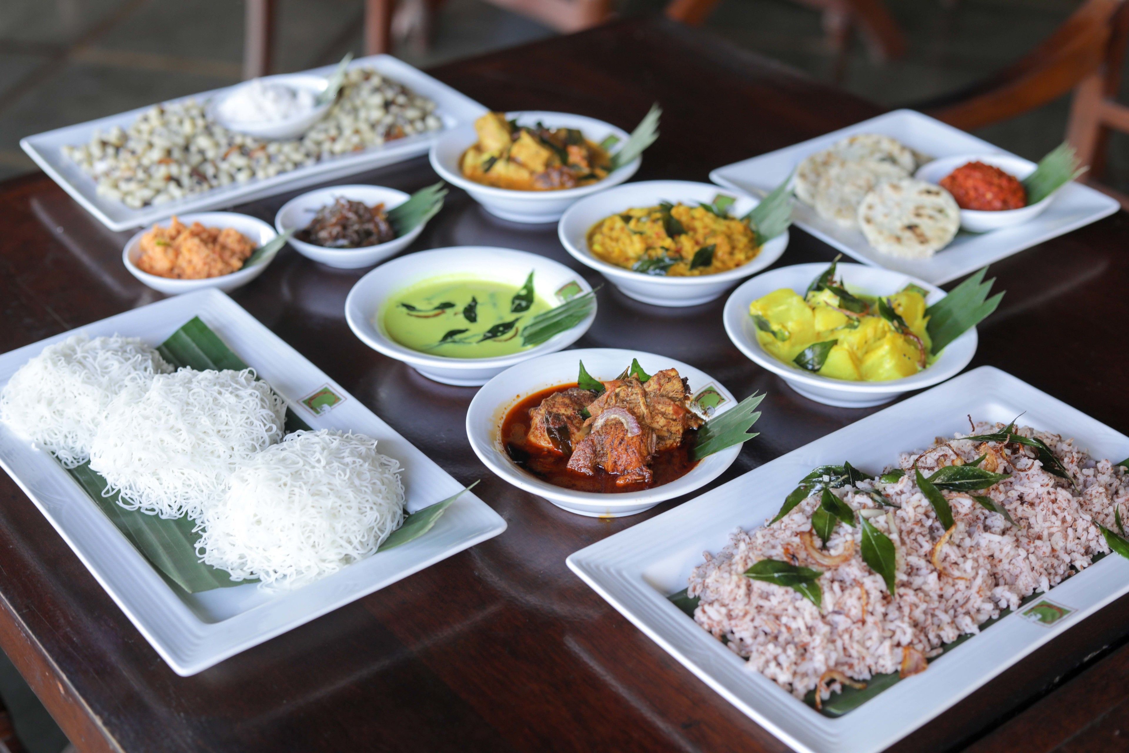 A table with various dishes, including rice and curries, arranged on white plates.