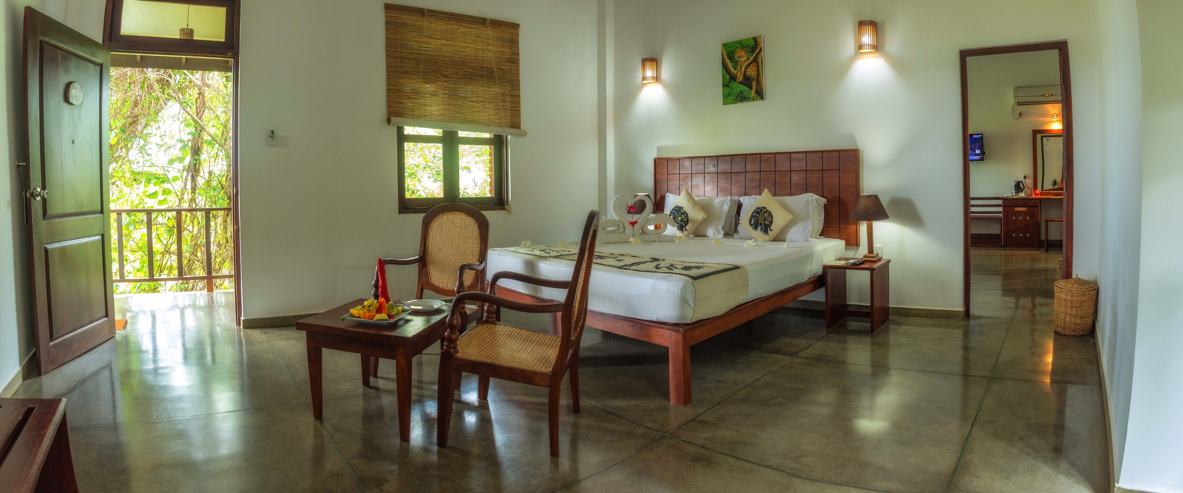 Un dormitorio con cama, mesitas de noche, una silla, una pequeña mesa con fruta y una ventana con vistas al verdor.