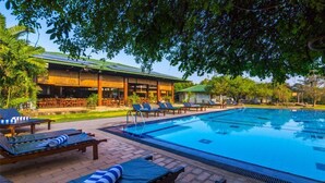 A swimming pool with lounge chairs, a covered seating area, and a building with a green roof. - Camellia Resort and Spa (Avudangawa)