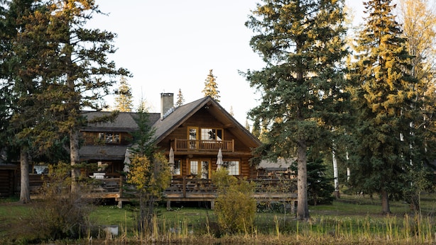 A log cabin with a deck and a pond in front. - Ten-ee-ah Lodge & Campground (Lac La Hache)