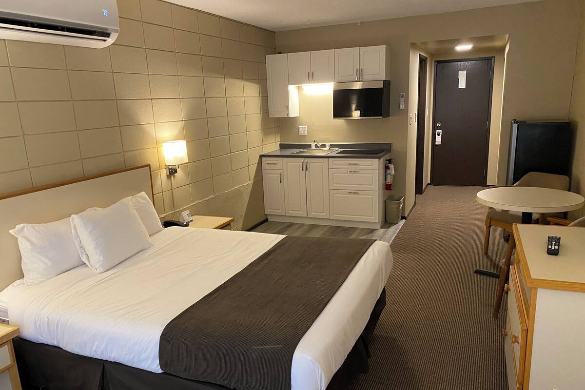A hotel room with a bed, a small kitchenette, a round table, and a TV.