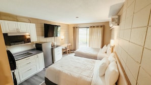 Habitación de hotel con kitchenette, dos camas, televisor y ventana con cortinas.