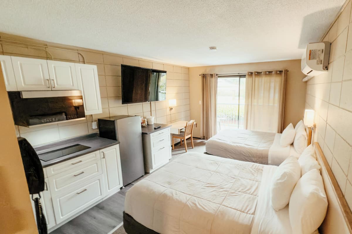 A hotel room with a kitchenette, two beds, a TV, and a window with curtains.