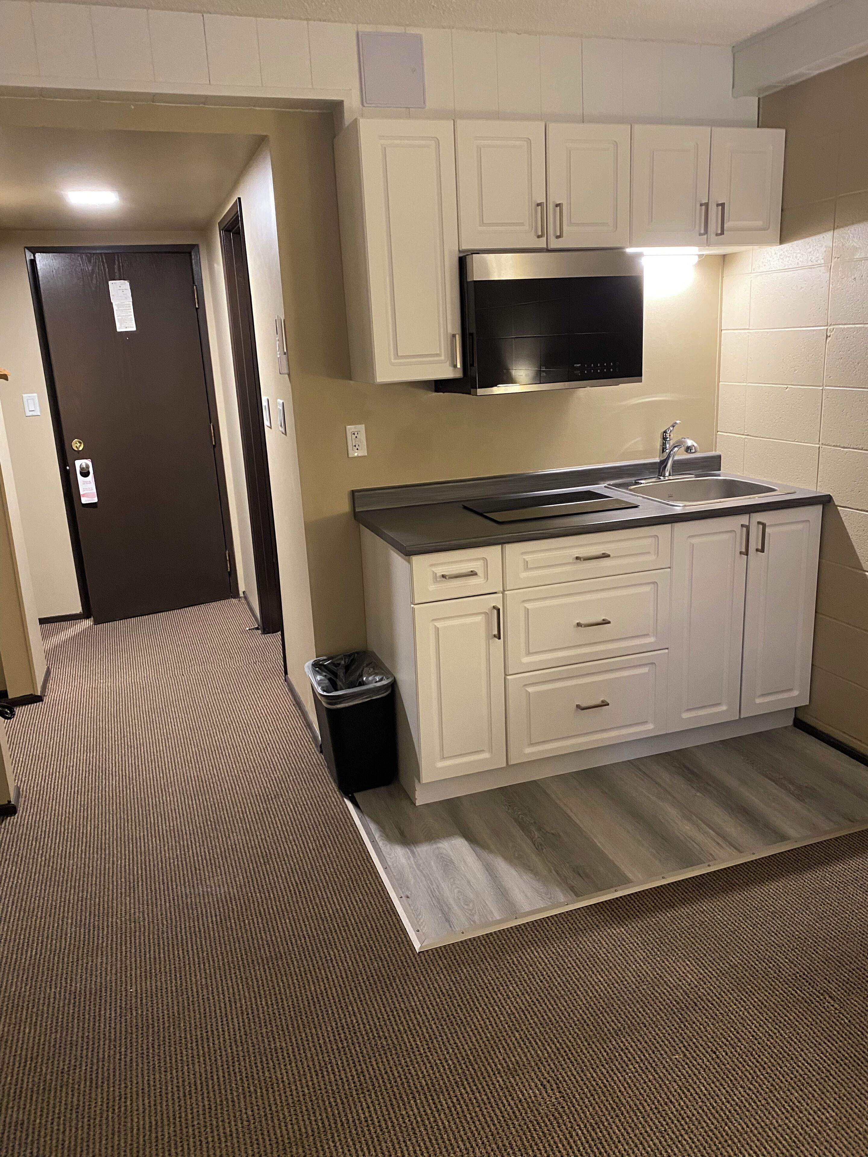 A compact kitchen with white cabinets, a stainless steel sink, and a black microwave.