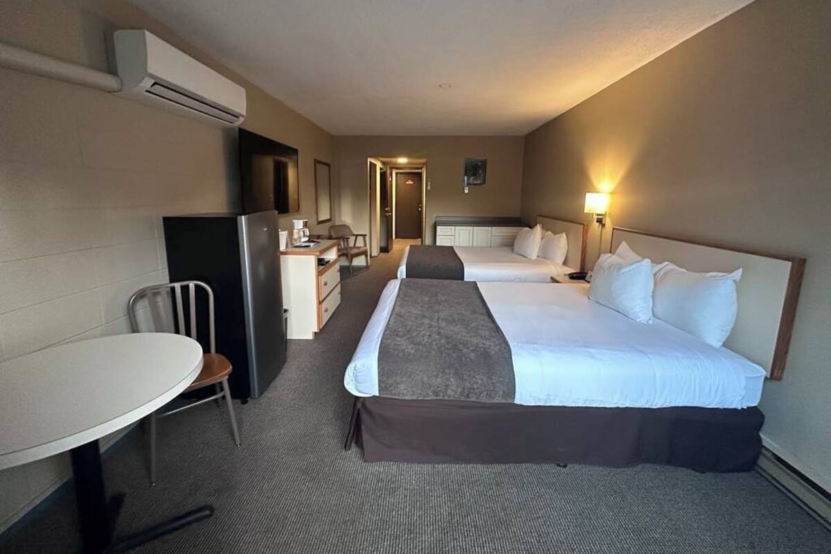 A hotel room with two beds, a desk, a chair, and an air conditioning unit.
