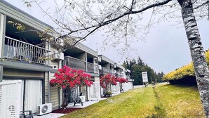 Un edificio residencial de dos pisos con balcón, unidades de aire acondicionado y un césped.