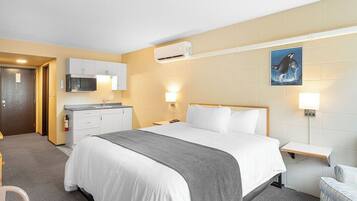 A hotel room with a bed, bedside table, lamp, air conditioning unit, and a painting on the wall.
