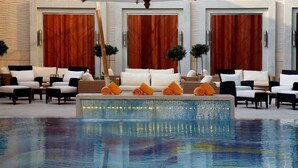 A poolside area with lounge chairs, a small table, and a decorative fountain. - Sands Macao (Macau)