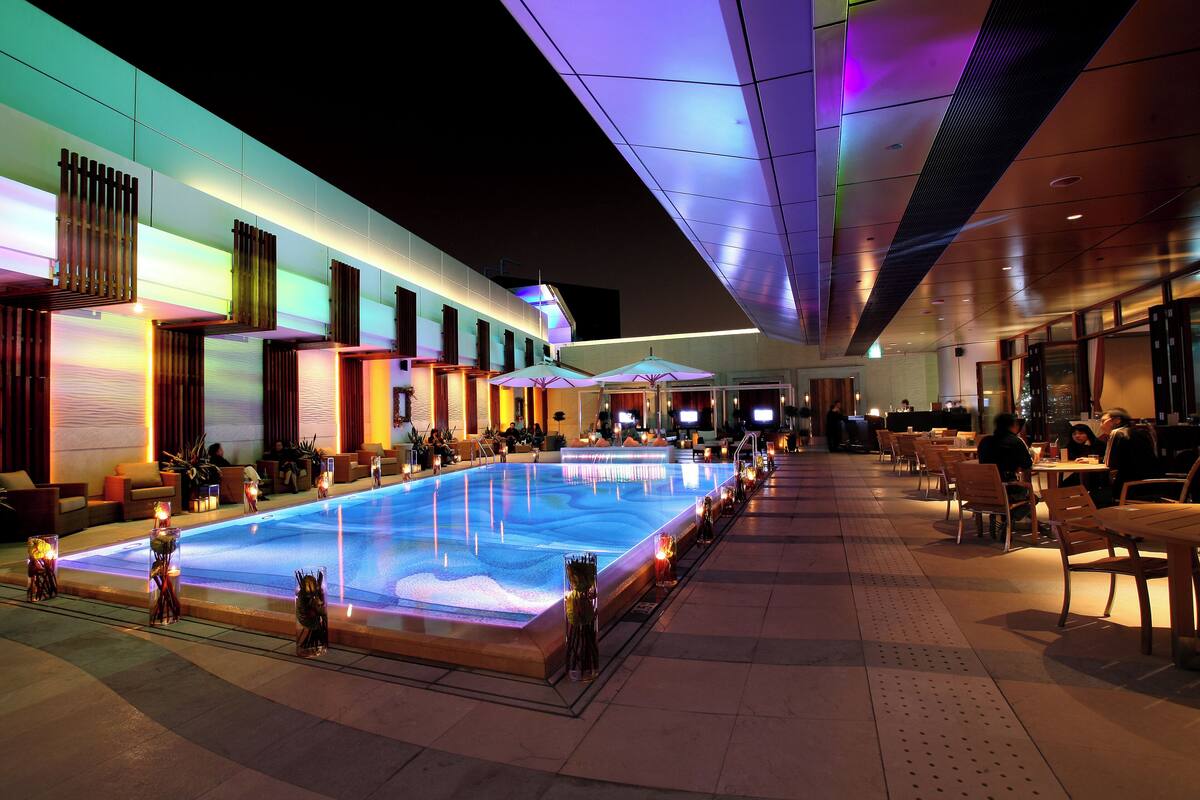 A pool area with seating and tables, surrounded by a modern building with large windows.