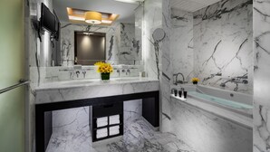 A modern bathroom with marble walls, a dual sink vanity, a large mirror, a built-in TV, and a bathtub. - Sands Macao (Macau)