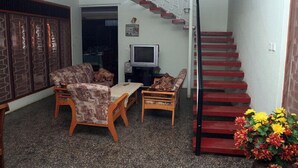 Una sala de estar con un conjunto de sofá, una mesa de centro y un televisor. Se ve una escalera con escalones rojos que conducen a un rellano.