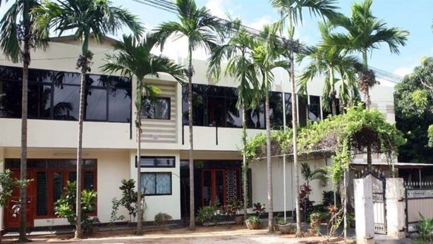 Un edificio de dos plantas con techo plano, varias ventanas y entrada protegida por una reja.