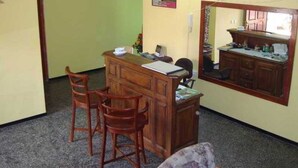 Una habitación pequeña y funcional con un escritorio de madera, dos sillas, un espejo y una kitchenette.