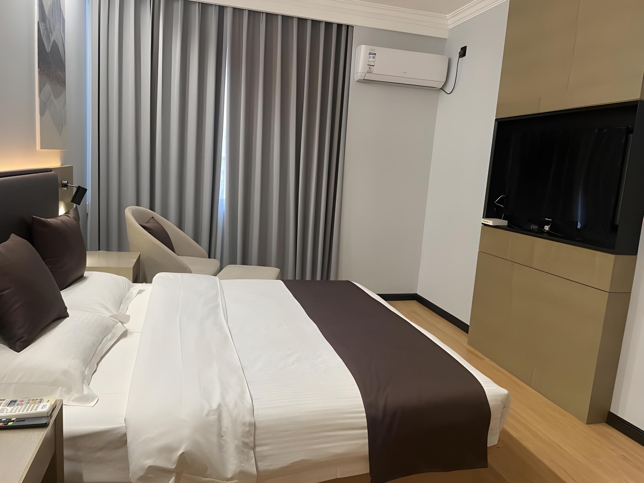 Una habitación de hotel con cama, escritorio con computadora, silla, televisor y aire acondicionado.