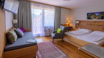 Ein Hotelzimmer mit einem Bett, einem Sofa, einem Sessel, einem kleinen Tisch mit einer Flasche, einem Fernseher und einem Bild an der Wand.