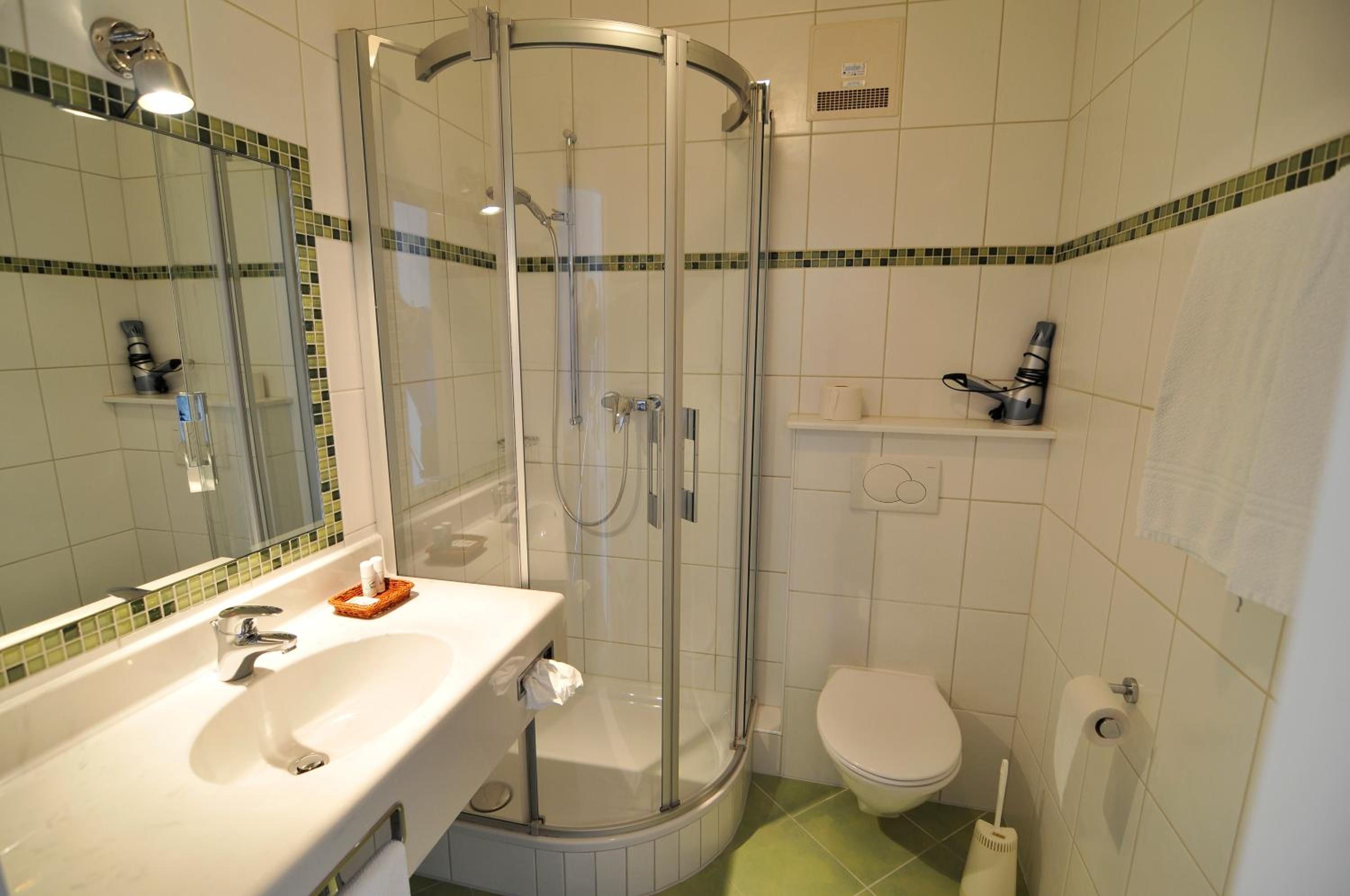 Un baño con ducha envuelta en cristal, un lavabo con artículos de aseo, inodoro y espejo.