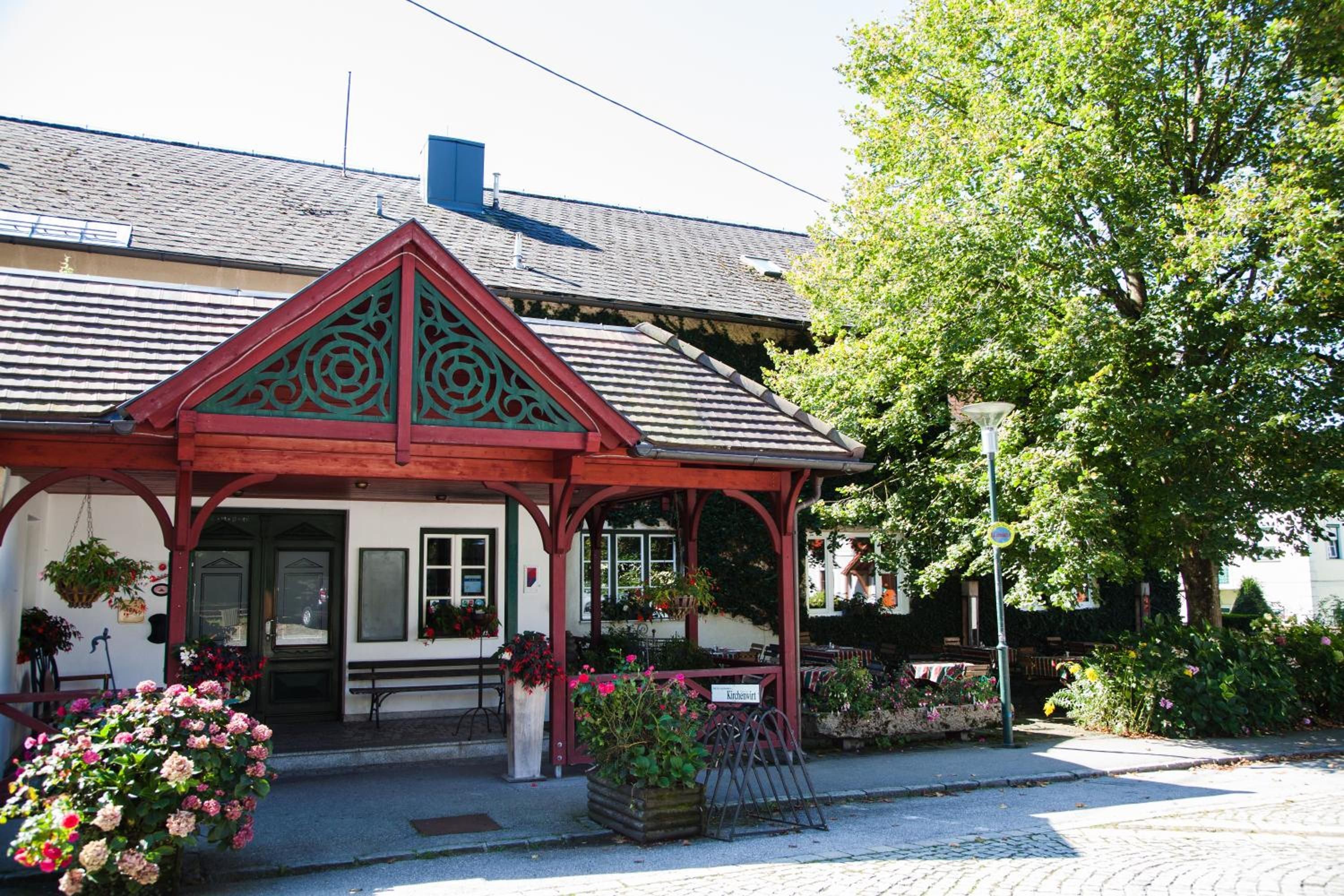 A traditional building with a red and white facade, a pitched roof, and a small porch with a sign that reads 'Kirchewei'.