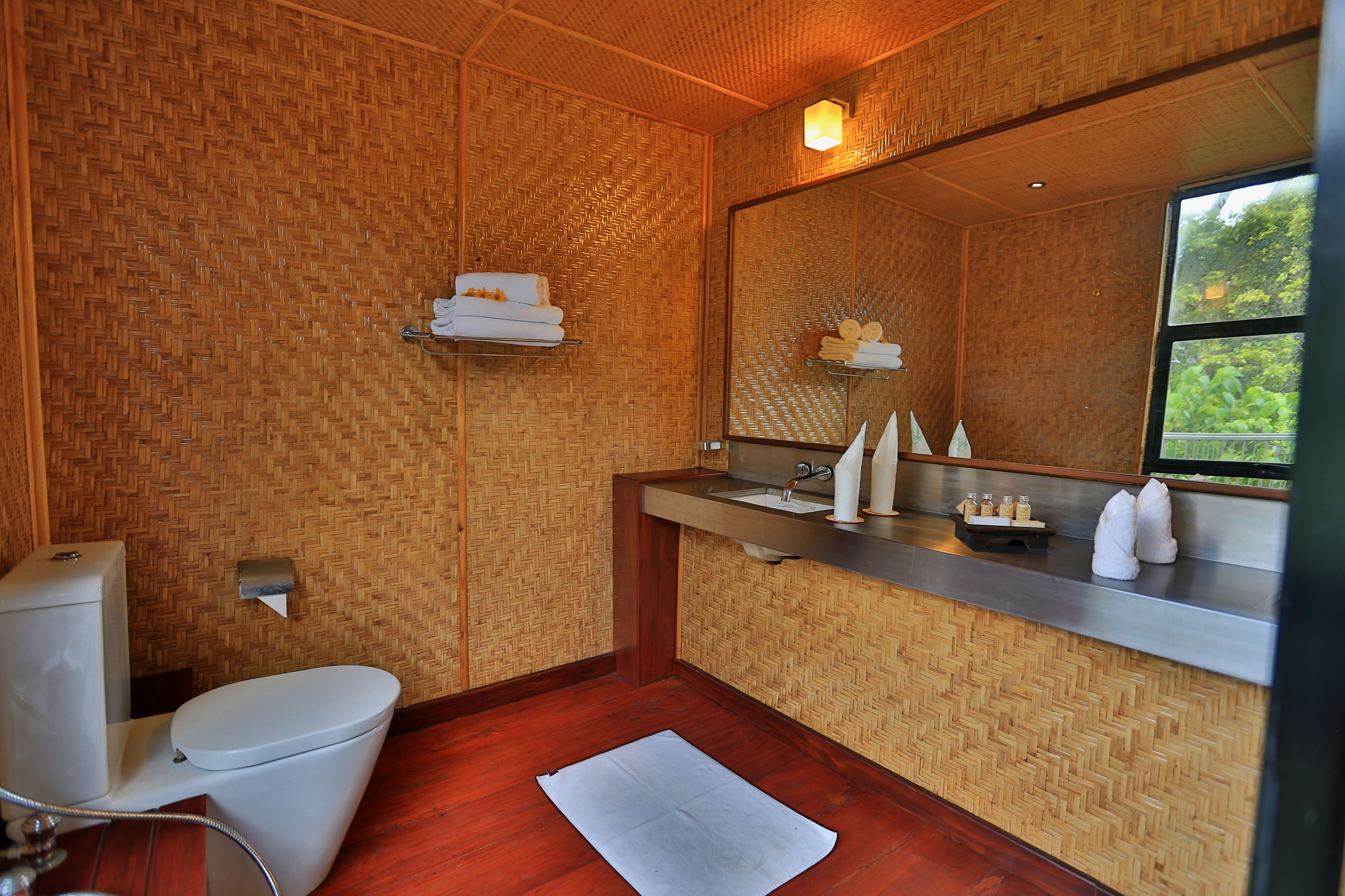 A bathroom with a wooden herringbone wall pattern, a white toilet, a sink with a mirror above it, and a window with a view of greenery.