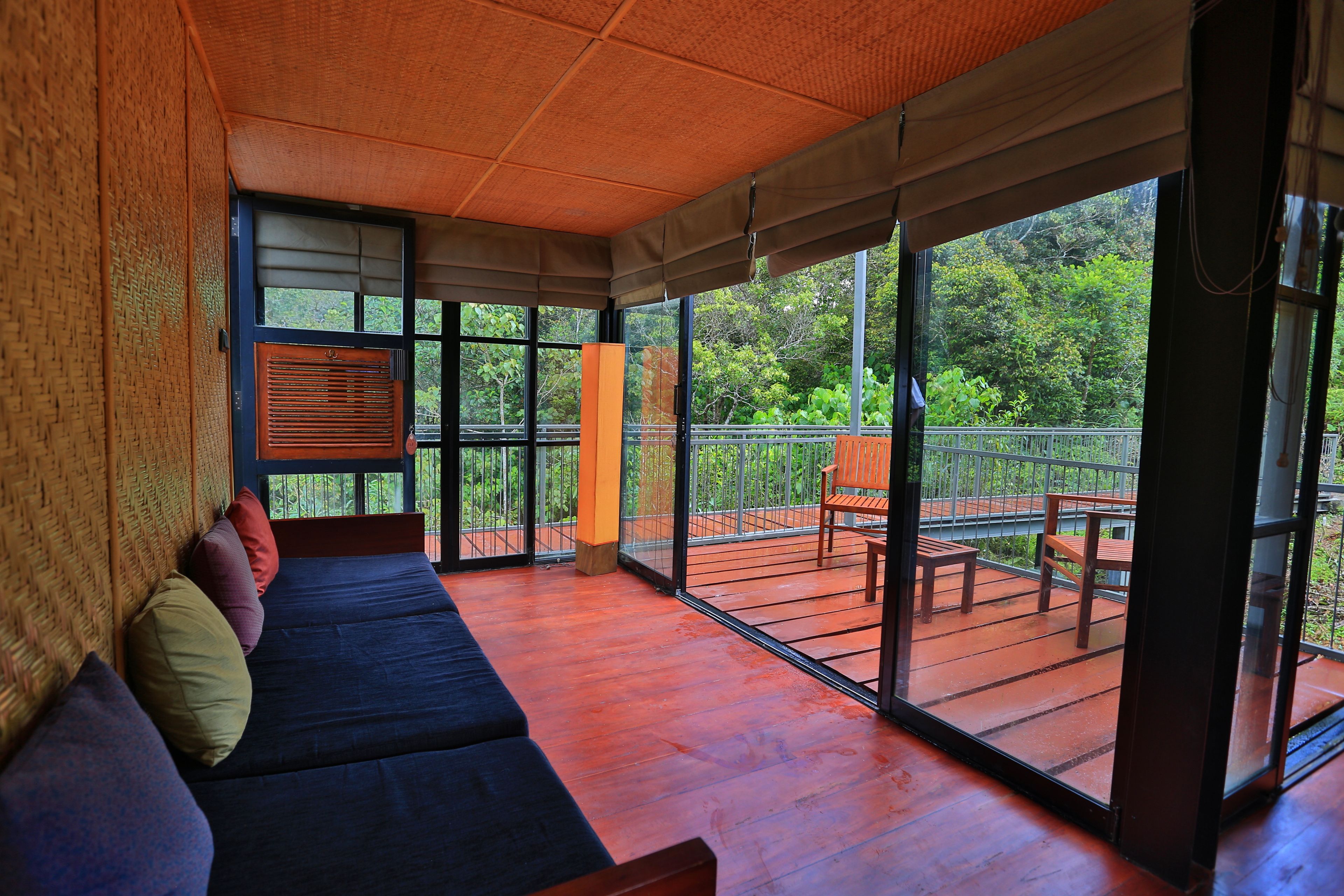 A room with a wooden floor, a sofa with cushions, a window, and a balcony with a railing and outdoor furniture.